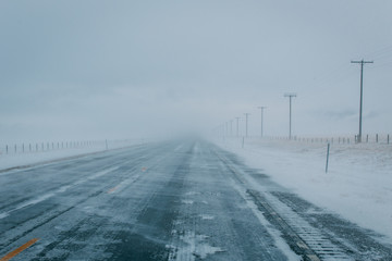 Obraz premium Road covered with snow during light snow storm with electricity poles along the road, in Montana, USA.