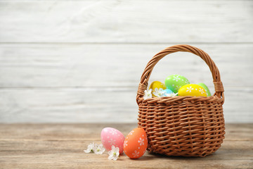 Colorful Easter eggs in basket and flowers on wooden table. Space for text