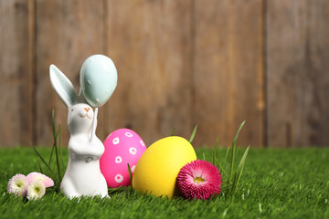 Colorful Easter eggs, rabbit and daisy flowers on green grass. Space for text