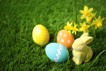 Fototapeta na wymiar Colorful Easter eggs, rabbit and narcissus flowers in green grass