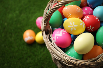 Fototapeta na wymiar Colorful Easter eggs in basket on green grass, closeup. Space for text