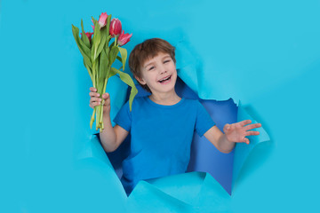 Fun child with bouquet of tulips poses through torn paper hole.  Effect of torn paper. mother's day