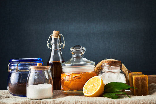 Eco-friendly natural cleaners: baking soda, soap, vinegar, salt, coffee, lemon and brush on table. Dark background.