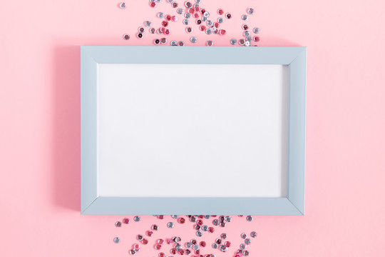 Festive pink background. Empty photo frame for text, confetti on light pink pastel background. Christmas. Wedding. Birthday. Flat lay, top view, copy space.