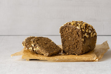 Dark oat flakes whole grain bread on a cutting board on grey background. Few slice near.  Isolated. Close up. Concept: healthy, vegan, vegetarian food, bakery. 