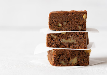 Stack of homemade chocolate brownie with nuts. Layer of paper bеtween it. Close up chocolate cake. Copy space. Grey background. Concept: pastry, American traditional dessert, bakery. 