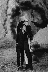 An Asian couple in love lit black smoke bombs in the mountains. Colored smoke. Black-white