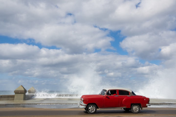 Classic red car driving through the streets of Havana waves splashing