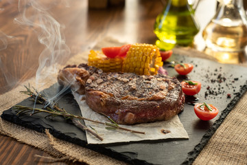 Steak with tomatos and corn on plate on wooden table