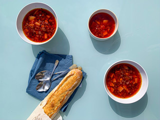Three bowls of borsch russian soup on a blue table. There are spoon and bread near it. Concept:healthy, vegan, traditional food. 
