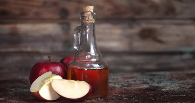 Apple cider vinegar is rotating on a wooden table.