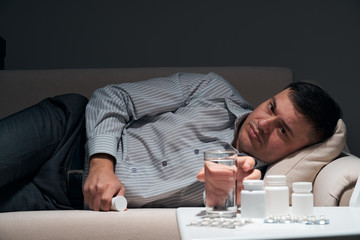 Overworked businessman is lying on the sofa and resting. Pills and glass of water near him.