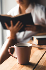 Woman in the morning drinks coffee and reads old book in a white shirt. Education, drink. manicure