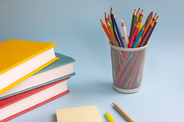 Fototapeta premium Back to school. A stack of books with multicolored covers , colored pencils, Notepad, and pen lie on a blue background. Concept of education. Selective focus