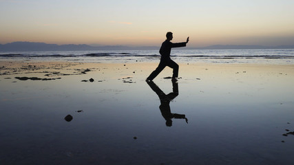 Silhouette of man practiceing qigong exercises at sunset by the sea - obrazy, fototapety, plakaty
