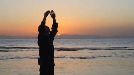 Silhouette of man practicing energy exercises at sunset by the sea - obrazy, fototapety, plakaty