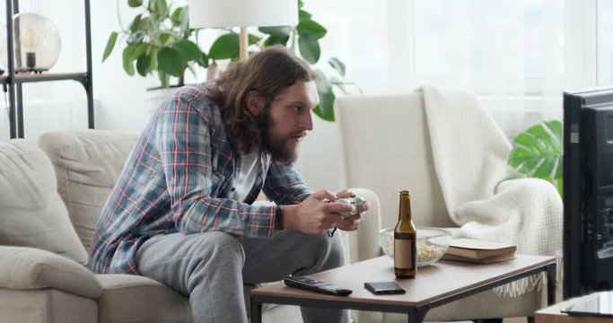 Man having food and drink while playing video game using joystick at home