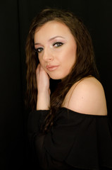 portrait of beautiful young brunette girl in studio with professional make up on black background, hands near face, bare shoulder, sensual expression, vertical image 