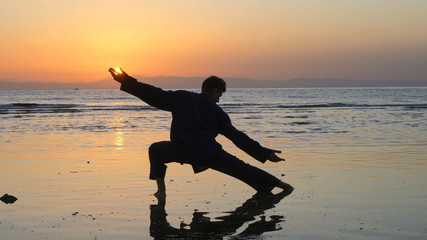 Silhouette of man practicing energy exercises at sunset by the sea