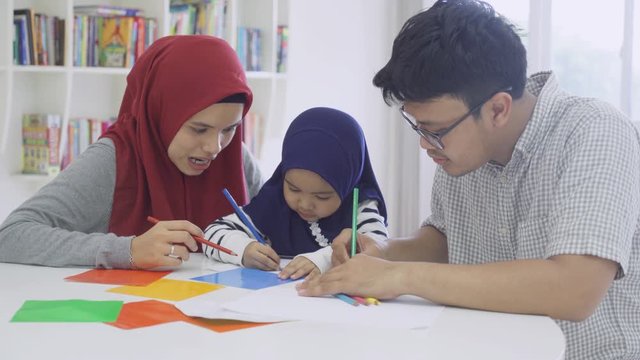 Two young muslim parents teaching their daughter for drawing on the paper at home. Shot in 4k resolution