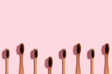 Geometric row of wooden toothbrushes on a pink background.