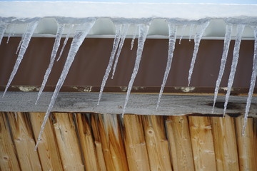 melting icicles hanging from a roof with drops of water falling down