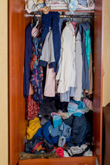 open wardrobe with clothes on hangers and clutter in open drawers