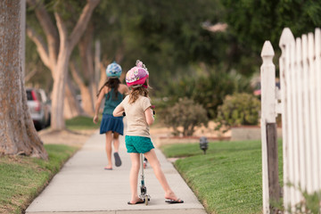Girls are wearing safety helmets while scootering on the sidewalk of their LA city.