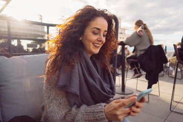 Millennial woman with a smart phone sit in a beautiful terrace. Casual lifestyles with technologies. Everyday fast internet connection to people. Winter and communication concept.