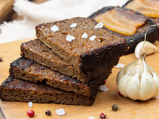 A stack of three croutons with ground pepper and one broken crouton in the foreground on a gray plate.