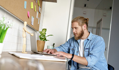 Young happy man student guy geek hipster freelancer work on project study online modern type email use laptop look at screen sit at desk table sticky notes, distant education home office concept.