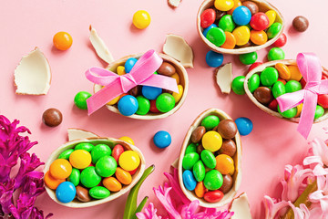 Chocolate Easter eggs and colorful candies on pink paper background. flat lay, top view, overhead, template, mockup.