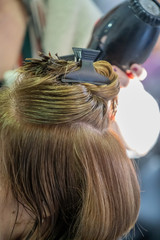 A vertical closeup shot of a hairdresser blow drying a woman's short hair in a beauty salon