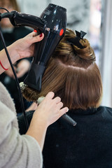 A vertical closeup shot of a hairdresser blow drying a woman's short hair in a beauty salon