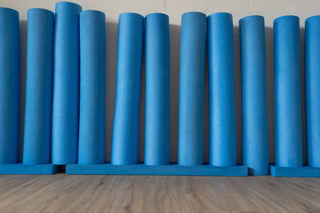 eleven blue rigid foam stem and Pilates rolls standing on wooden oak floor against the white brick wall. Pilates Roll for balance- and stabilisation exercises. Low angle view.
