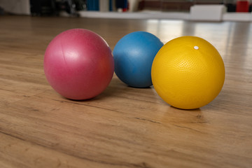 Three small and colorful gymnastic balls on wooden floor of a gymnastic hall of a group fitness center.
