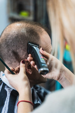 A vertical closeup shot of a woman cutting a man's hair in the barbershop