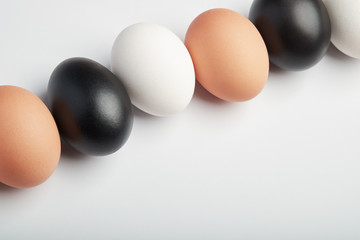 Row of eggs of different colors on a white background. Black, white and brown chicken eggs.