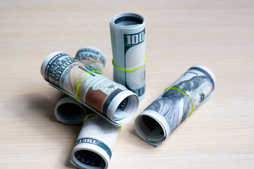 one hundred dollar bills knitted by elastic in rolls on a light wooden table. side view. to close