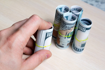 one hundred dollar bills with hand tied with an elastic band into rolls on a light wooden table. side view. to close