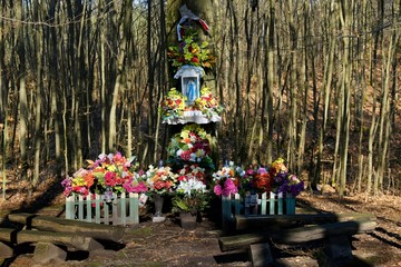The chapel with the Virgin Mary on the tree in the forest is beautifully decorated with colorful flowers. Kashubia, Poland