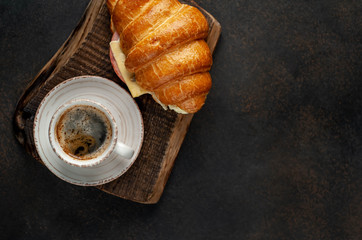 Coffee and croissant with sausage, cheese and salad on a stone background, with copy space for your text. Breakfast concept