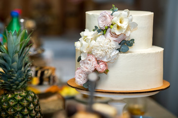 Tall sweet wedding cake decorated with live pink and white flowers on a table.