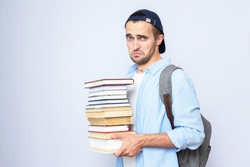 Upset student guy with a stack of books, portrait, gray background, copy space, toned