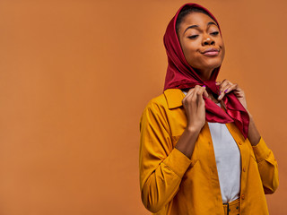 Concentrated woman in a yellow shirt ties a red scarf on her head by hands. Fashion concept