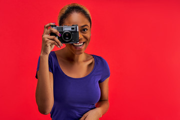 Happy woman in a blue T-shirt with hair gathered in a bun takes a photo on old camera. Photo concept