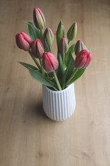 Red tulip flower bouquet on a white pot on a wooden surface