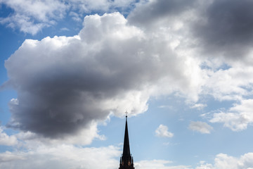 A church and a cross on top visible through the clouds at the bright blue sunny sky