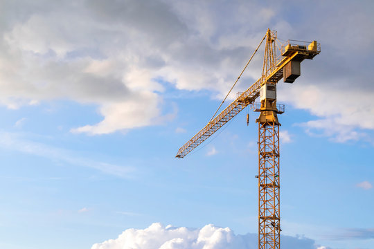 Construction vehicles hoisting tower cranes against a blue sky in an industrial city landscape. Industrial background with tower crane silhouettes and free space for text.