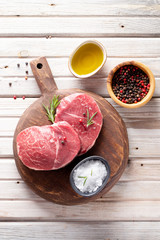 Raw steak Parisienne of marbled beef on a dark wooden cutting board, seasoning salt and pepper, olive oil on the wooden table. Top view.